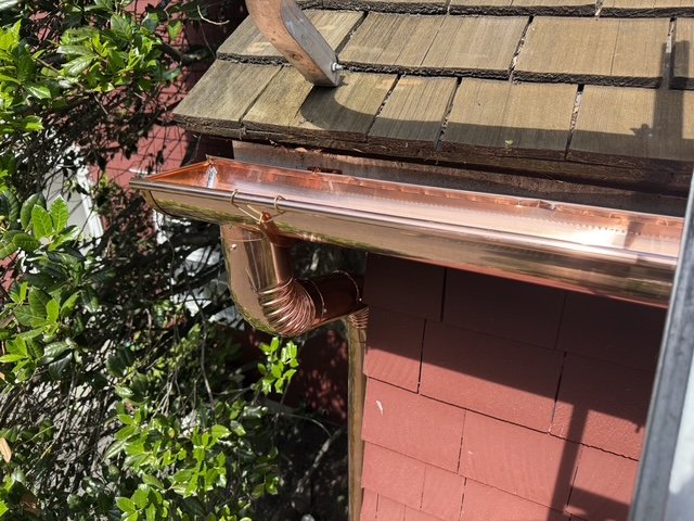 Installed copper gutter and downspout beside a cedar roof